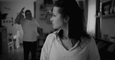 Kadın hararetli tartışmalar sırasında yüzünü geri çeviriyor. Arka plandaki adam duygusal hareketler yapıyor. Gerilime ve gergin ilişki dinamiklerine odaklanıyor..