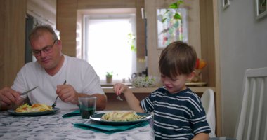 Aile masada bir yemeği paylaşır, anne bulaşıkları servis ederken baba ve oğul doğal sohbetler yapar, bağlantıyı ve sıcaklığı ön plana çıkarır.