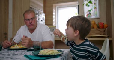 Baba ve oğul aile yemeği sırasında masada birlikte yemek yiyorlar, özgün bir bağ sergiliyorlar ve rahat bir yuva ortamında günlük aile hayatı sergiliyorlar.