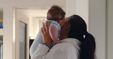 Anne koridorda bebeğini yüzüne yakın kaldırıyor, doğal ışık, sıcak ve sevgi dolu aile anı, samimi otantik yaşam tarzı, beslenme ve bağ kurma sahnesi..