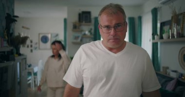 Erkek, tartışma sırasında yoğun bir ifadeyle kameraya bakıyor, kadın oturma odasında, gergin ve duygusal bir ilişki çatışması ve hüsran anı yaşıyor..