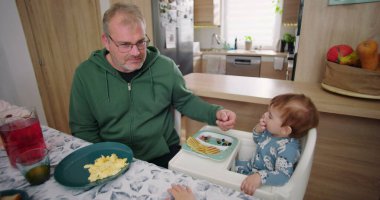 Baba, ufaklığın renkli kahvaltı tabağını meyve ve gözlemelerle keşfetmesine yardım ediyor.