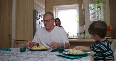 Aile masada bir yemeği paylaşır, anne bulaşıkları servis ederken baba ve oğul doğal sohbetler yapar, bağlantıyı ve sıcaklığı ön plana çıkarır.