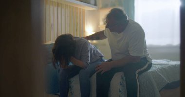 Kocası üzgün karısına destek oluyor, yatağın kenarında oturuyor, duygusal mücadeleye odaklanıyor, zihinsel sağlık farkındalığı, umutsuzluk, üzüntü ve kişisel kriz temaları