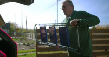 Adam arka bahçedeki araba bagajına katlanmış bir merdiven yerleştiriyor, dış görevlere ya da ev bakımı projelerine hazırlanıyor, organizasyon ve kamu hizmetlerine odaklanıyor