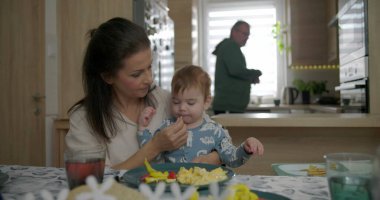 Anne kahvaltı masasında bebeği besliyor, bebekle kaynaşıyor çırpılmış yumurta ve sebzeleri keşfediyor, sıcak mutfak ortamında aile bağlarını besliyor.