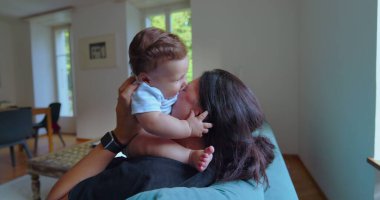 Anne ve bebek, parlak bir oturma odasında birlikte oynuyorlar. Neşeli anlar, kahkahalar ve doğal ışıklandırmayla bağ kuruyorlar.