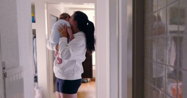 Anne koridorda karoları yansıtarak bebeği tutuyor, samimi otantik yaşam tarzı sahnesi, samimi aile anı, beslenme ve bağ kurma, sıcak ve doğal ışık