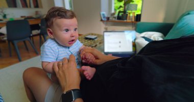 Annesinin kucağında oturan, gözleri şaşkın ve meraklı bir bebeğin yakın çekimi, onunla sakin, aile ortamında etkileşime giriyor..