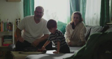 Anne ve baba kanepede oturup çocuğa gülümsüyor kahve masasında oyuncak trenle oynuyor rahat oturma odası düzeninde, neşeli aile anları, kapalı alanda kaynaşma zamanı.