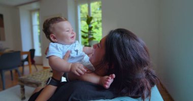 Anne ve bebek, parlak bir oturma odasında birlikte oynuyorlar. Neşeli anlar, kahkahalar ve doğal ışıklandırmayla bağ kuruyorlar.