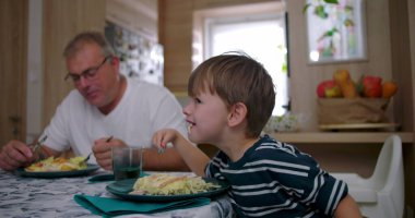 Baba ve oğul aile yemeği sırasında masada birlikte yemek yiyorlar, özgün bir bağ sergiliyorlar ve rahat bir yuva ortamında günlük aile hayatı sergiliyorlar.