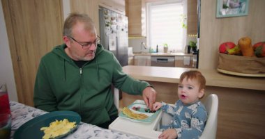 Baba, ufaklığın renkli kahvaltı tabağını meyve ve gözlemelerle keşfetmesine yardım ediyor.