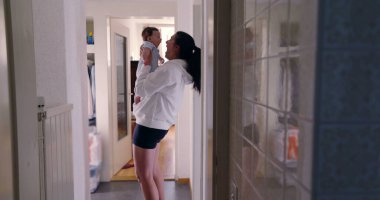 Anne koridorda karoları yansıtarak bebeği tutuyor, samimi otantik yaşam tarzı sahnesi, samimi aile anı, beslenme ve bağ kurma, sıcak ve doğal ışık