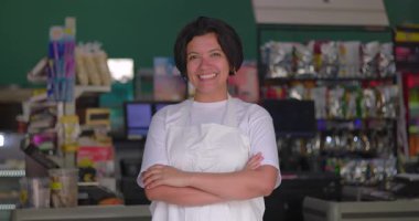 Süpermarkette önlük takan gülümseyen Latin kadın. Renkli özgüvenli portre, neşeli iç mekan perakende seti.
