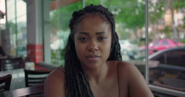 Ciddi bir Afro-Amerikalı kadın restoran masasında oturuyor. Düşünceli bir ifadeyle kapalı mekan portresi çiziyor. Şehir manzaralı pencerenin yanında sıradan bir manzara.