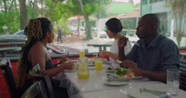 Çeşitli arkadaşlar restoranda yemek yiyor, evde rahat yemek yiyor, doğal ışık ve parlak şehir manzarası ile canlı sohbetler yapıyor.