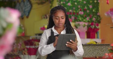 Afro-Amerikalı çiçekçi tablet hakkındaki bilgileri inceliyor, odaklanma ve profesyonellikle çiçekçilik görevlerini yönetiyor