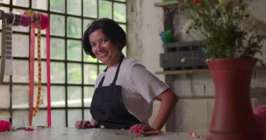 Kırsal kesimdeki çiçekçide neşeli bir şekilde gülümseyen kadın, küçük işletme sahibi, olumlu tavır ve yaratıcı çevreye olan güvenini dile getiriyor.