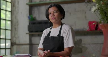 Kırsal bir çiçekçinin içinde düşünceli bir şekilde duran kadın çiçekçi, küçük işletme sahibi yaratıcı projeleri ve iş yerindeki gelecekteki hedeflerini yansıtıyor.