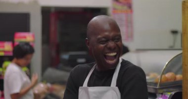 Önlüklü, neşeli, Afro-Amerikan şarküteri işçisinin arkası yumuşak Latin bir bayan müşteriyle market tezgahının önünde gülümsemesini kapatın.