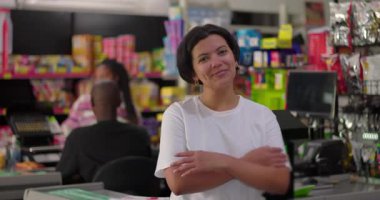 Etrafı ürünler ve insanlarla çevrili Bakkal Bakkalında duran kolları çaprazlanmış kendine güvenen Latin Alışverişci