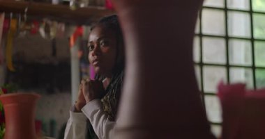 Çiçekçinin içinde çiçeklerin arkasında sessizce düşünen kadın çiçekçi, küçük işletme sahibi gelecekteki hedeflerini ve iş zorluklarını yansıtıyor