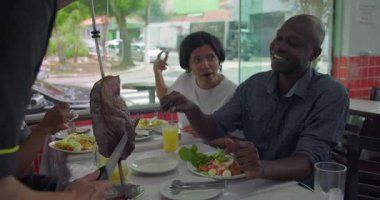 Restoran masasında gülen ve taze yemek yiyen arkadaşlar doğal ışık ve şehir ortamında rahat bir atmosferle keyifli bir ev yemeği deneyimi.