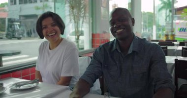 Restoran masasında birlikte oturan sırıtan farklı arkadaşlar, kapalı alanda yakalanan neşeli an, doğal ışık ve şehir manzaralı neşeli atmosfer