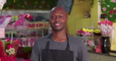 Çiçekçinin içinde kendine güvenen bir çiçekçi, renkli buketler, çiçek aranjmanları ve hediye süslemeleri arasında gülümseyen küçük bir işletme sahibi.