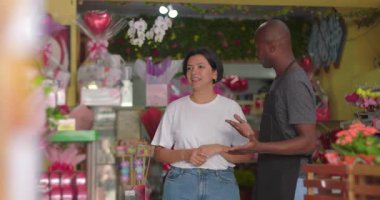 Çiçekçi dükkanında kadınlara mavi orkide veren bir adam. Çiçekçi, çiçeklerle dolu canlı bir mağazada müşterilere taze çiçekler sunuyor.