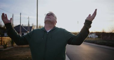 Dışarıdaki adam kollarını havaya kaldırmış, yukarıya bakıyor, minnettarlığını ve umudunu ifade ediyor, kırsal alanda ruhani bir an, sakin ve sakin, günbatımı atmosferi.