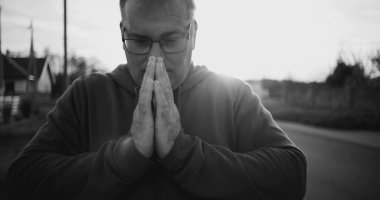 Elleri duada sıkışmış, başı eğik, derin düşüncelere dalmış, huzurlu kırsal alan, siyah beyaz, ruhani an, yansıma ve minnettarlık dolu bir adam.