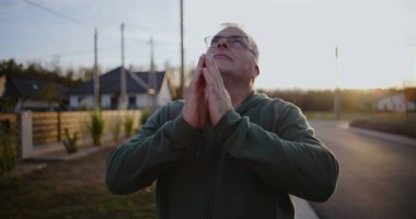 Dışarıdaki adam kollarını havaya kaldırmış, yukarıya bakıyor, minnettarlığını ve umudunu ifade ediyor, kırsal alanda ruhani bir an, sakin ve sakin, günbatımı atmosferi.