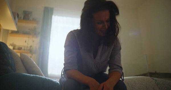 Женщина с головой в руках, сидя на кровати в эмоциональном стрессе, частный и отражающий момент, борясь с грустью или стрессом, приглушенное внутреннее освещение