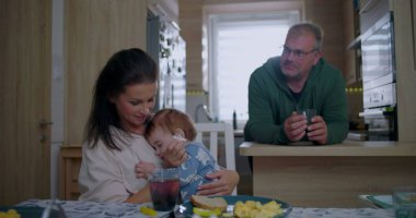Anne, bebeği yemek masasının yanında tutarken baba da mutfaktan, sıcak ve sıcak bir evde aile ortamını gözlemliyor..