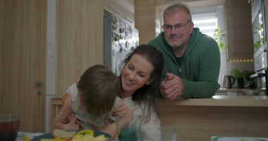 Anne büyük çocukla yemek masasında gülerken, baba izliyor, neşeli aile anı sıcak yuva ortamında bağ ve mutluluk yaratıyor.