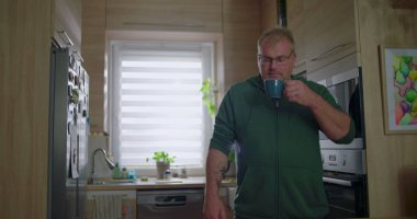 Mutfaktaki mavi bardaktan içen adam, sabah rutini, sıcak içecekten hoşlanan sıradan bir ev hayatı, rahat bir an, dekorlu modern bir mutfak ortamı.