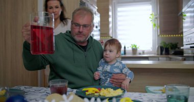 Anne ve babanın aile yemeği sırasında bebeği büyütmesi, yemek masasında renkli yiyecek ve içeceklerle sıcak ve neşeli bir etkileşim, sıcak ve sevgi dolu bir ev ortamı yaratması.