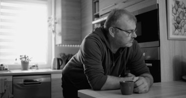 Mutfak tezgahına dayanan adam, düşünceli ifade, sabah içkisi, monokromatik stil, modern ev dekorasyonu, doğal ışık ile günlük ev hayatı