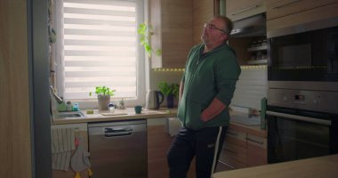 Adam mutfak tezgahına yaslanıyor, elleri cepte, modern mutfak arka planı, günlük rutin işler, düşünceli anlar, yeşillik ve dekorasyon.