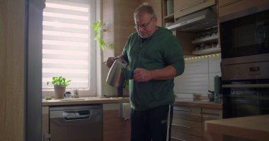 Adam bardağa sıcak su dolduruyor, mutfak aktivitesi, ev hayatı, ev hayatı, modern mutfak düzeni, odaklanmış ifade, ev ortamında sıradan bir an.