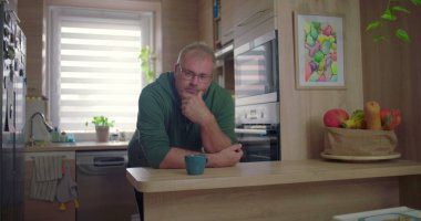 Modern mutfakta içki içen bir adam, rahat ev anı, günlük sabah rutini, ev ortamında yeşillik ve güneş ışığı, rahat yaşam tarzı.