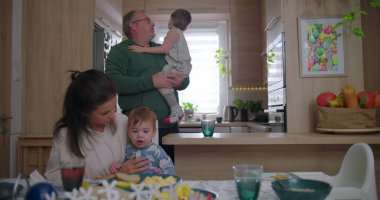 Baba kucağında bebek, anne elinde fincanla gülümserken aile sıcacık bir mutfak ortamında sıcacık bir anın tadını çıkarıyor..