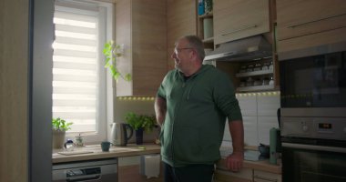 Mutfakta eli kalçasında, derin düşüncelere dalmış, sıradan bir hayat tarzı olan, modern bir mutfak geçmişi olan, evde boş vakti olan, düşünceli bir adam.