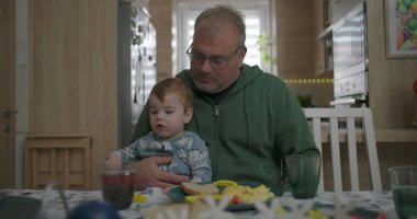 Baba kucağında bebekle yemek masasında, sıcak bir yuva ortamında aile yemeği sırasında şefkatli ve şefkatli bir anı besliyor.