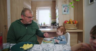 Aile yemek masasında birlikte kahvaltı yapıyor, anne bir bardak meyve suyu tutuyor, baba çocuklara yardım ediyor, sevgi ve sevgi besliyor.