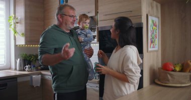 Anne kucağında bebeğini besliyor, baba sıcak mutfakta özenle izliyor, aile ortamını, sevgiyi ve birlikteliği gösteriyor.