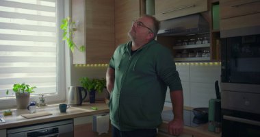 Mutfak penceresinden bakan adamın yakın çekimi, yansıtıcı ruh hali, günlük yaşam tarzı, modern ev ortamı, düşünceli ifade, aile ortamında kişisel zaman.