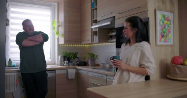 Kadın ve erkek modern bir mutfakta dikilip gündelik sohbetlerin tadını çıkarıyor ve parlak ve davetkar bir şekilde kahve içiyorlar.